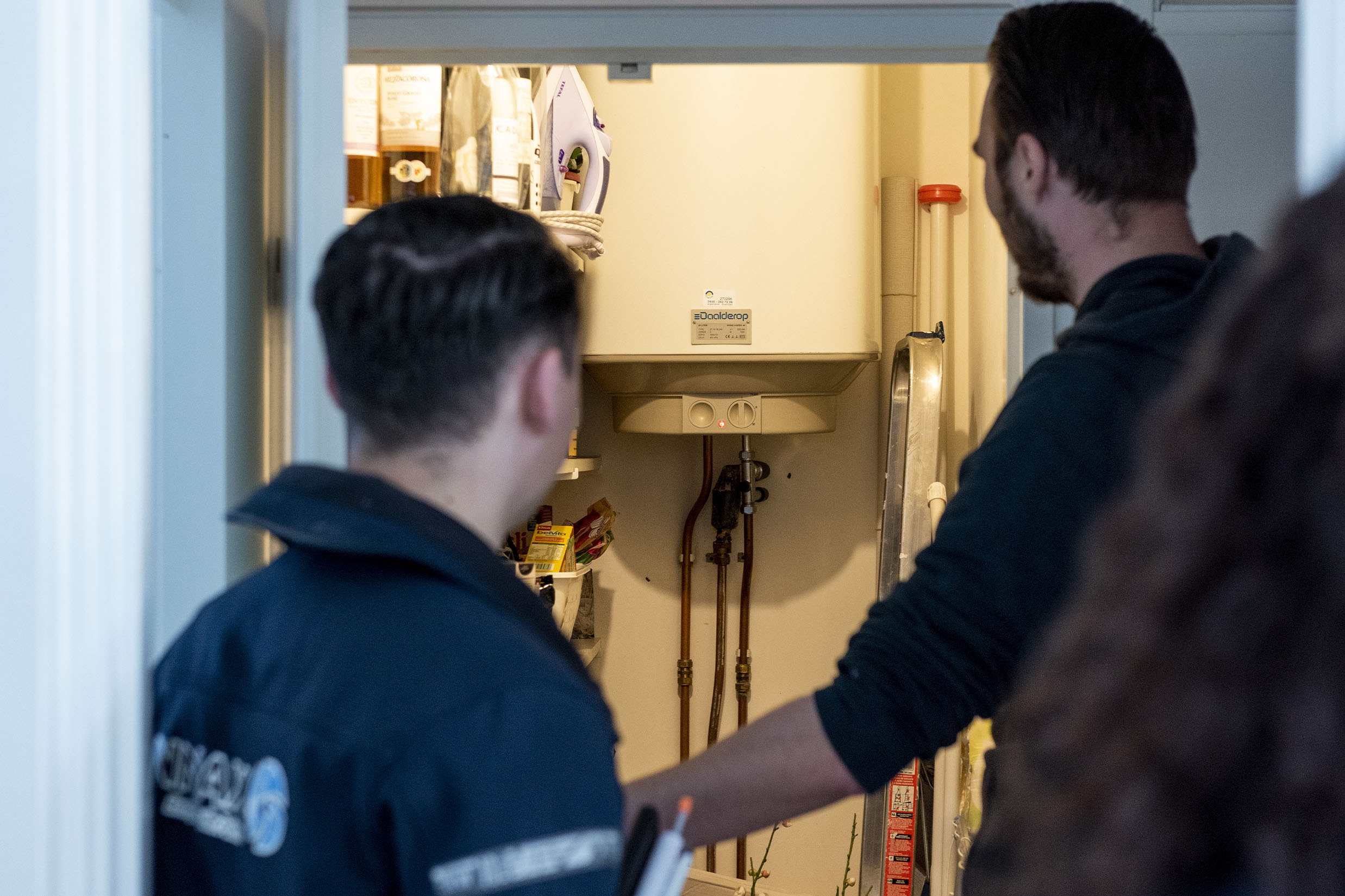 Een inspecteur kijkt met een bewoner mee naar de boiler tijdens een keuring.